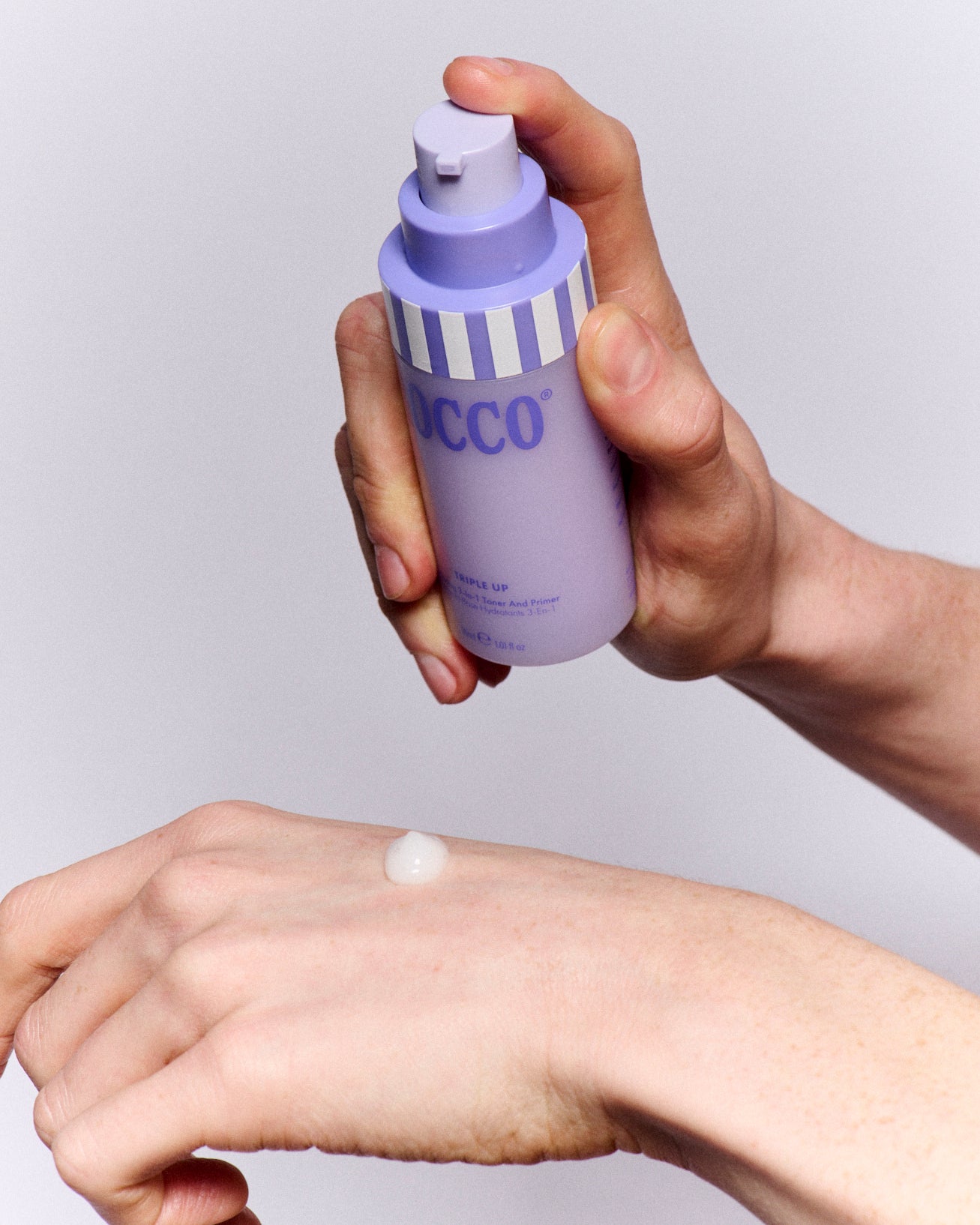 Hand holding a Triple Up purple bottle labeled 'ROCCO' applying cream to the wrist against a light background