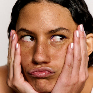 Close-up of a woman with hands on her face against a plain background