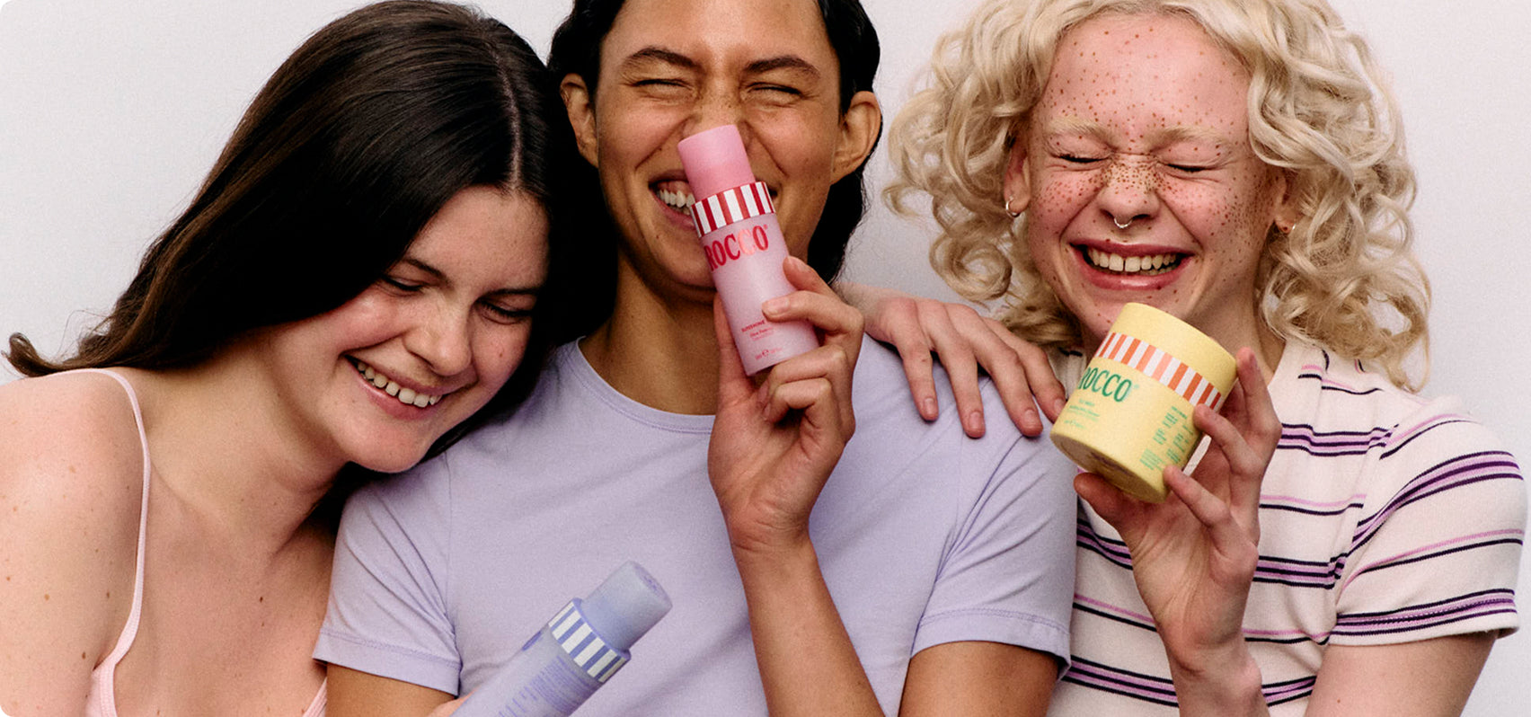 Three people holding and showing off skincare products against a plain background