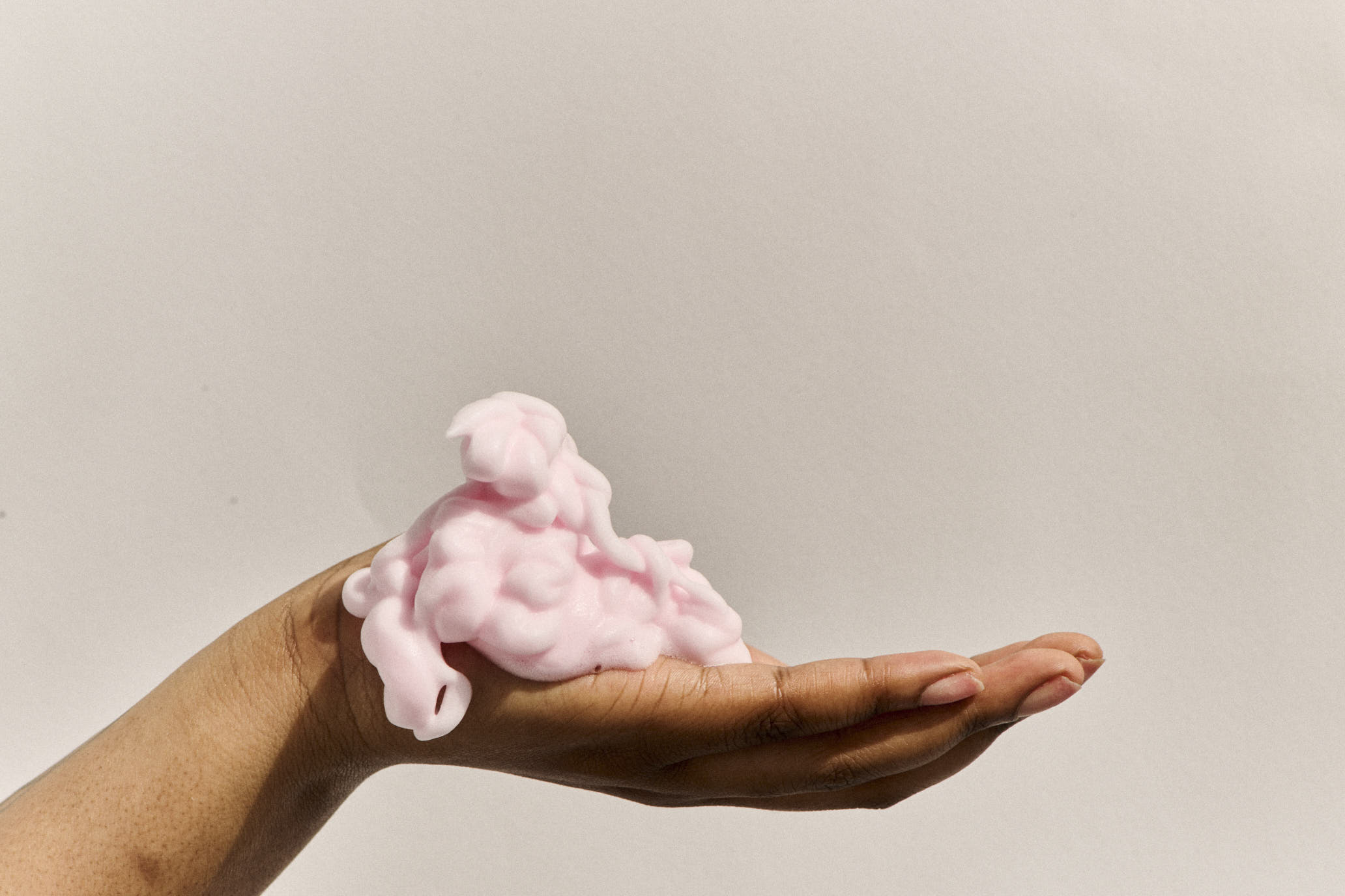 Hand holding pink foaming cleanser substance against a plain background