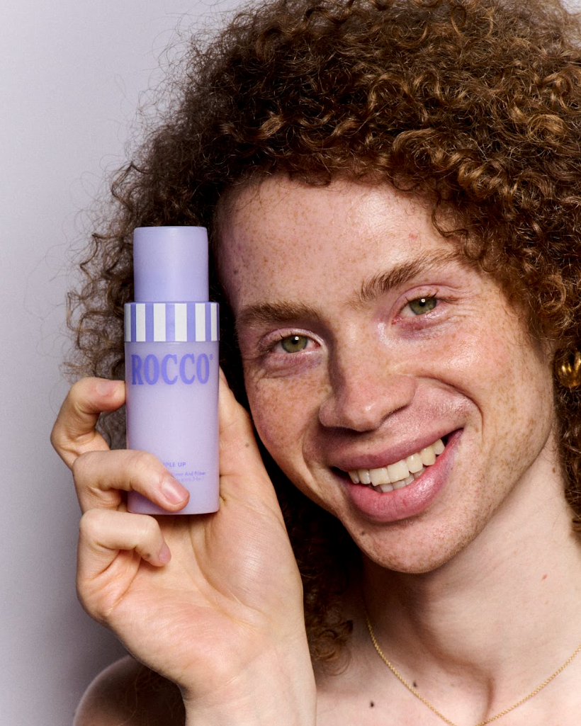 Person holding a purple bottle labeled 'ROCCO Triple Up' against a plain background