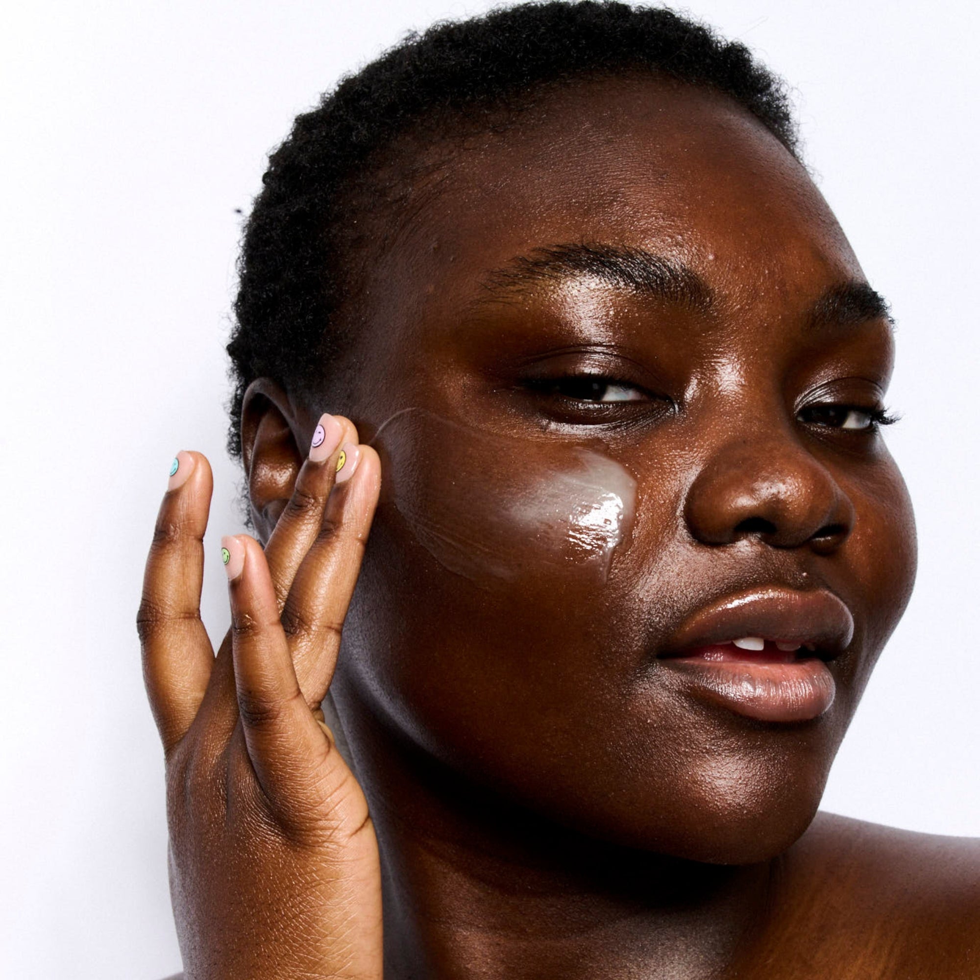 Close-up of a person applying skincare product to their face on a white background