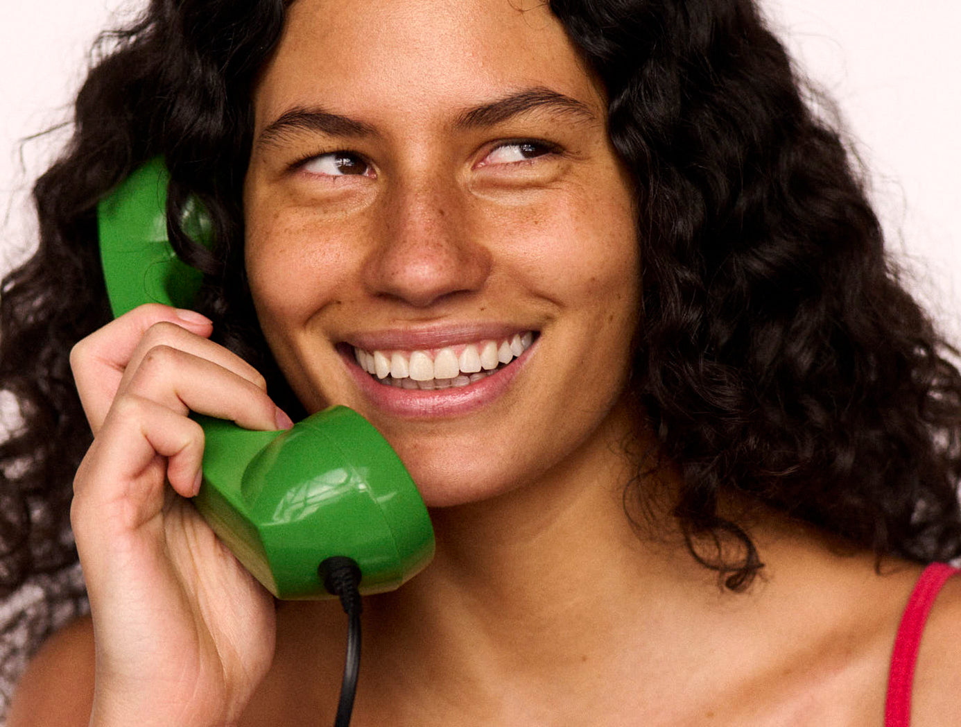 Woman holding a green phone to her ear with a smile on her face.